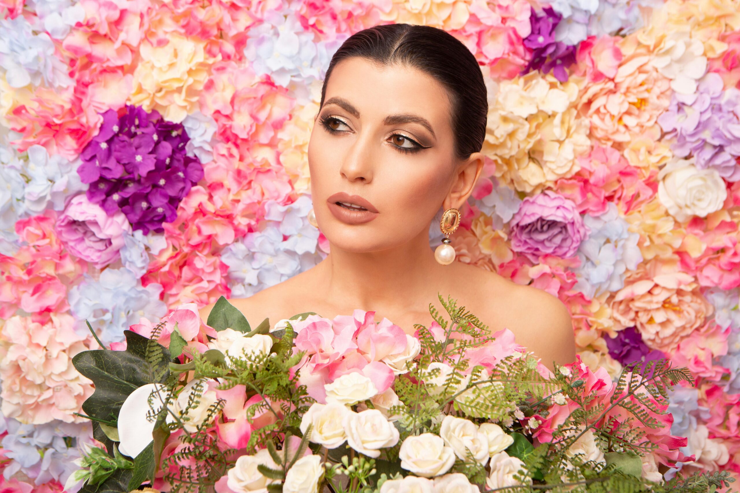 A stylish woman with pearl earrings amidst a colorful floral backdrop, exuding elegance and grace.